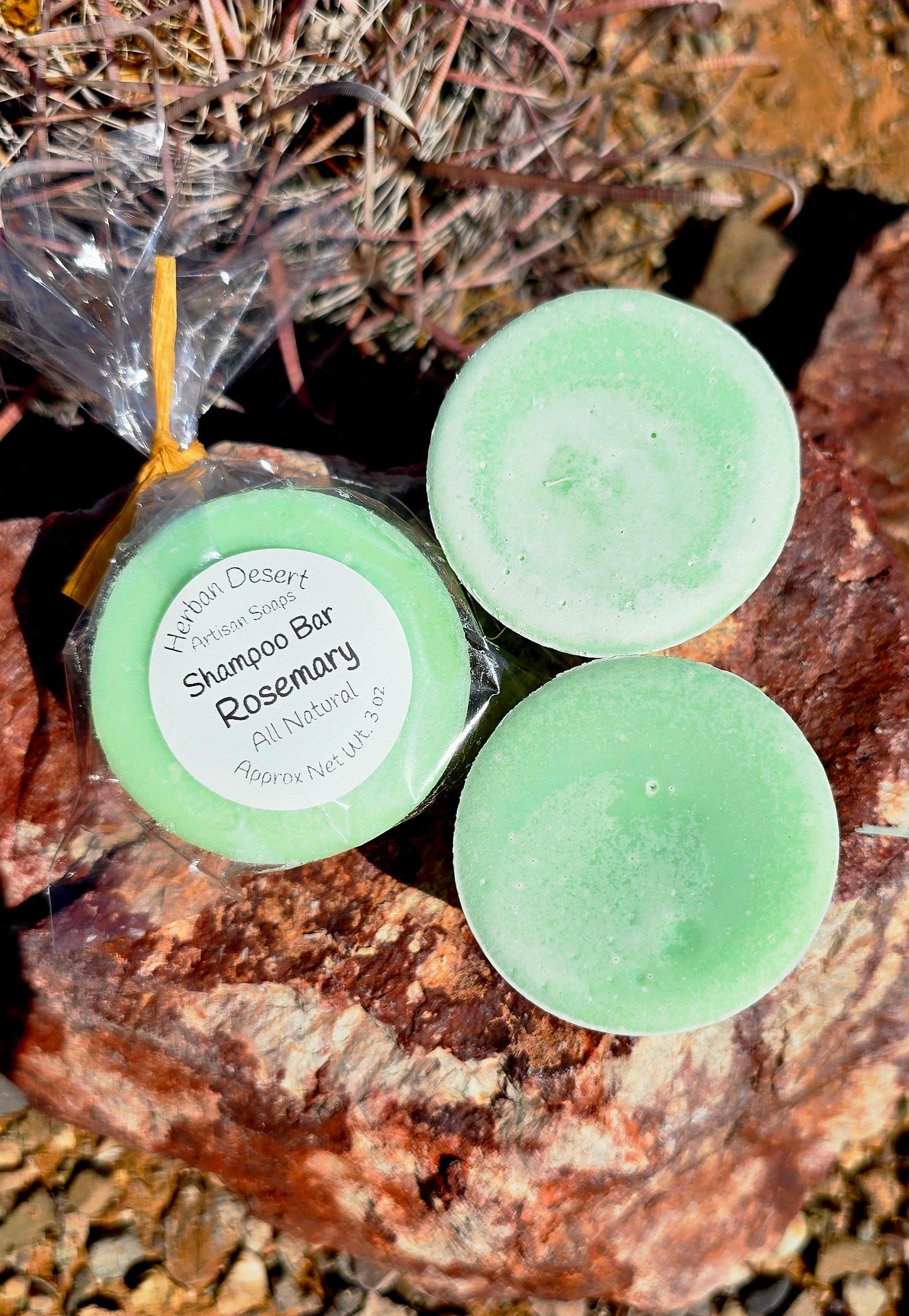 Three bars of Herban Desert's rosemary shampoo bars. One is wrapped in clear plastic with a ribbon and our label. The other two are unwrapped.