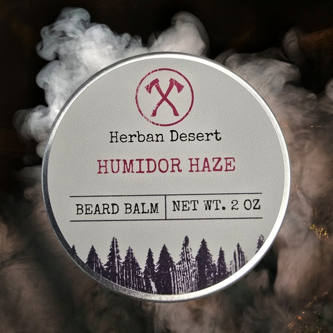 A container of Humidor Haze Beard Balm by Herban Desert with a smoky background, featuring a label with the product name and weight.