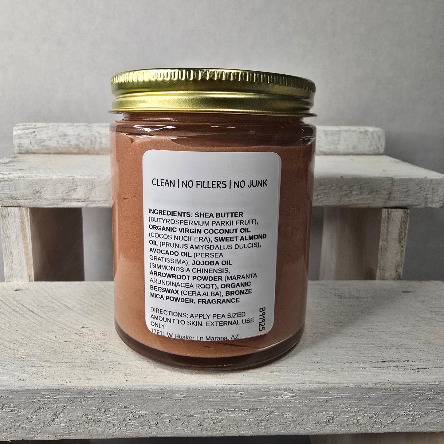 Jar of Herban Desert cinnamon sugar glow body butter showing ingredient panel and gold lid on a wooden block against a gray background.