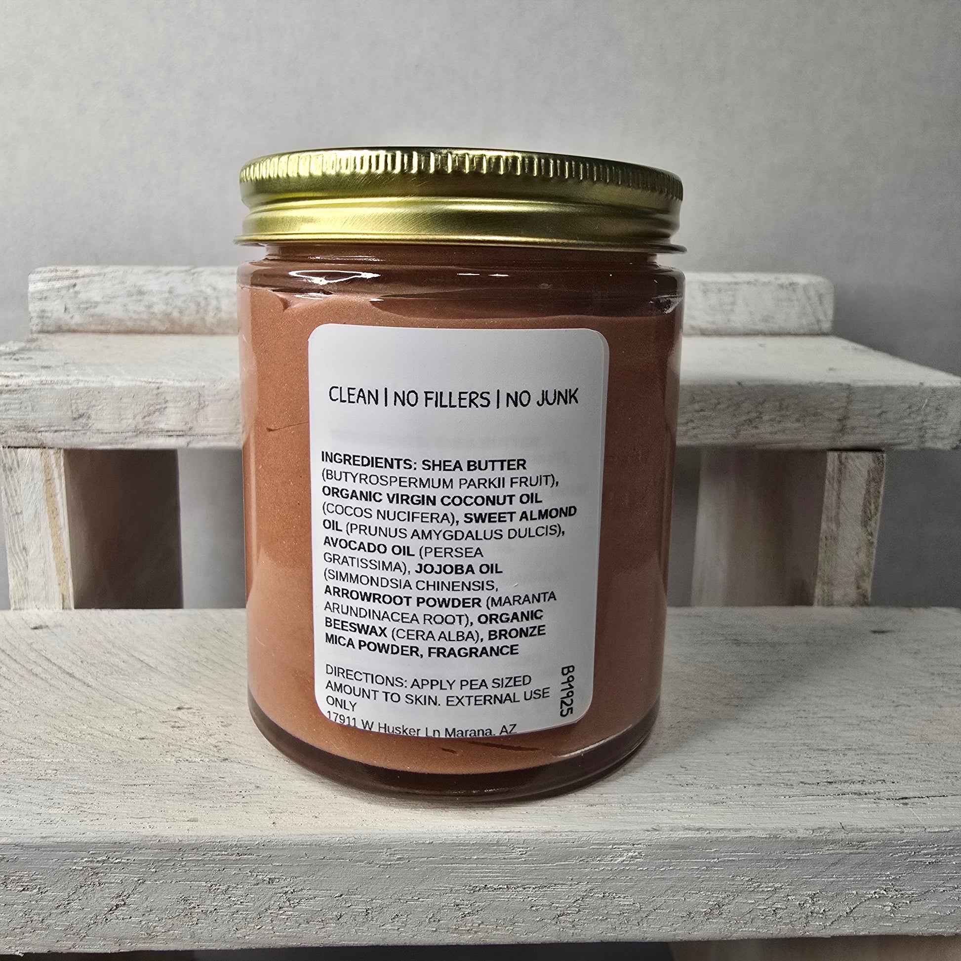 Jar of Herban Desert cinnamon sugar glow body butter showing ingredient panel and gold lid on a wooden block against a gray background.